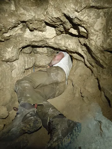 Explorateur progressant à plat ventre dans une chatière étroite creusée dans la roche