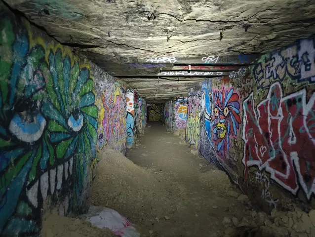 Couloir étroit aux deux parois couvertes de graffitis, dominé par une gueule de monstre verte