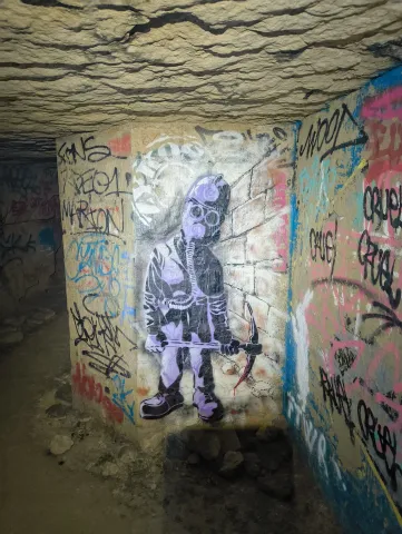 Pochoir violet d'un enfant squelette tenant un arc, peint sur un pilier au milieu des tags