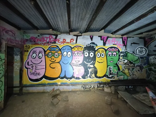 Fresque de personnages ronds et colorés alignés sur le mur d'une salle à poutres