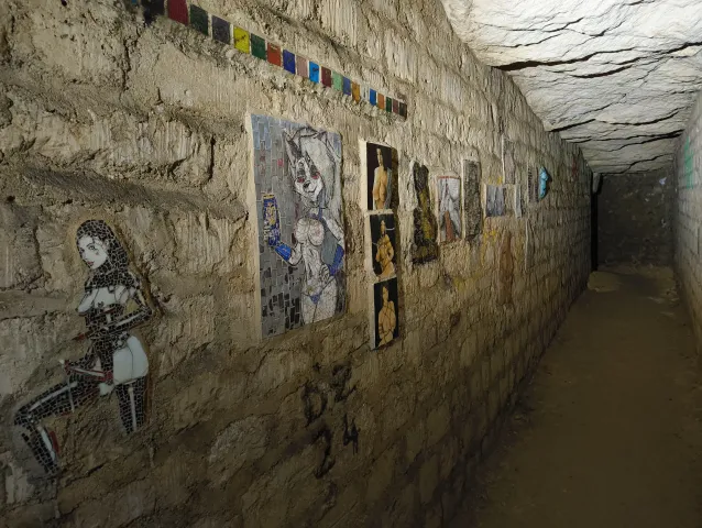 Série d'œuvres encadrées accrochées le long d'un mur de pierre, en galerie d'exposition souterraine