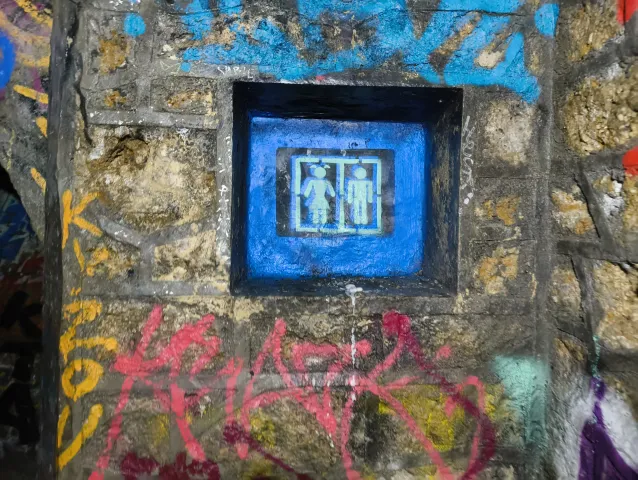 Petite niche peinte en bleu abritant deux silhouettes, encastrée dans un mur de pierre taggé