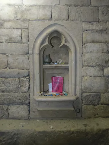 Niche gothique sculptée dans un mur de pierre appareillée, garnie de bougies et d'offrandes