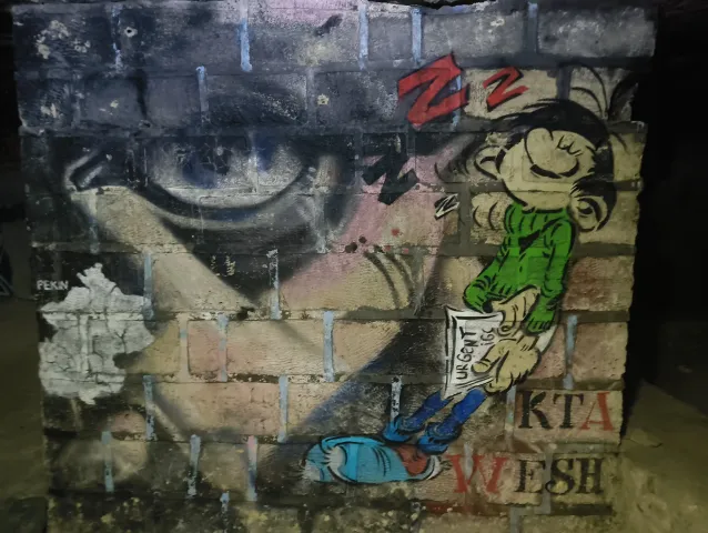 Graffiti d'un œil géant et d'un personnage de bande dessinée endormi sur un mur de briques peint