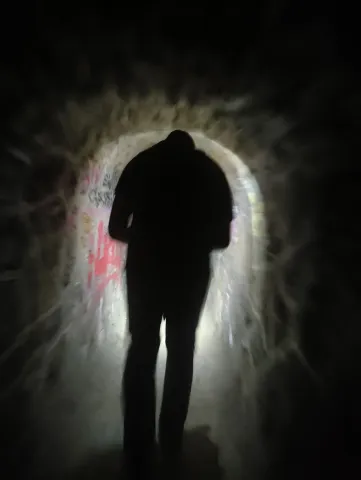 Silhouette d'un explorateur à contre-jour dans une galerie, cerné d'un halo de lumière