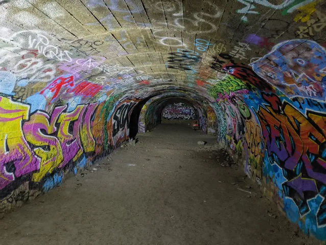 Galerie voûtée entièrement recouverte de graffitis colorés, s'enfonçant dans l'obscurité